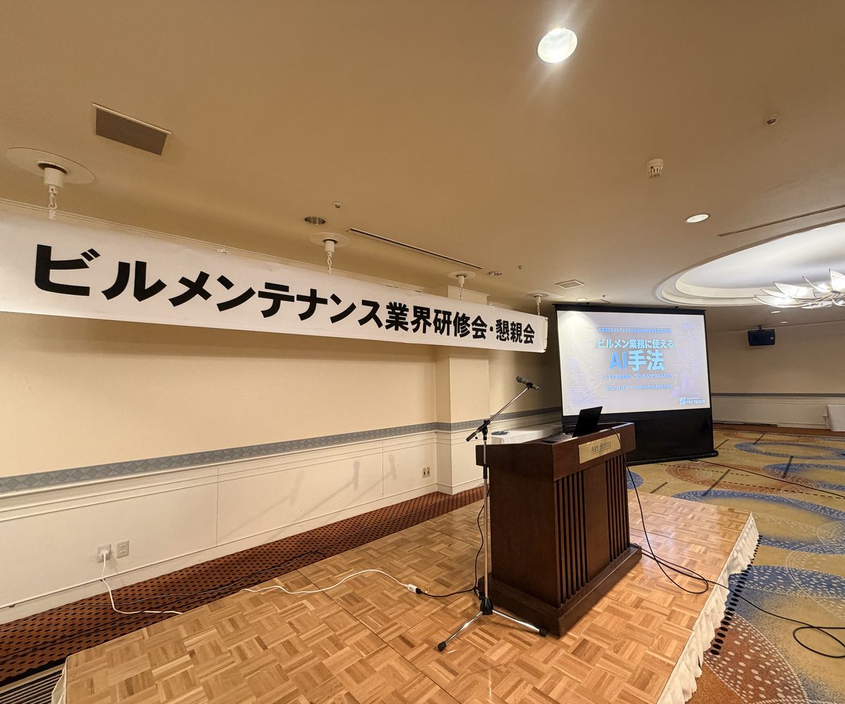 ビルメンテナンス業界研修会の会場。横断幕と、AI手法をテーマにした投影資料