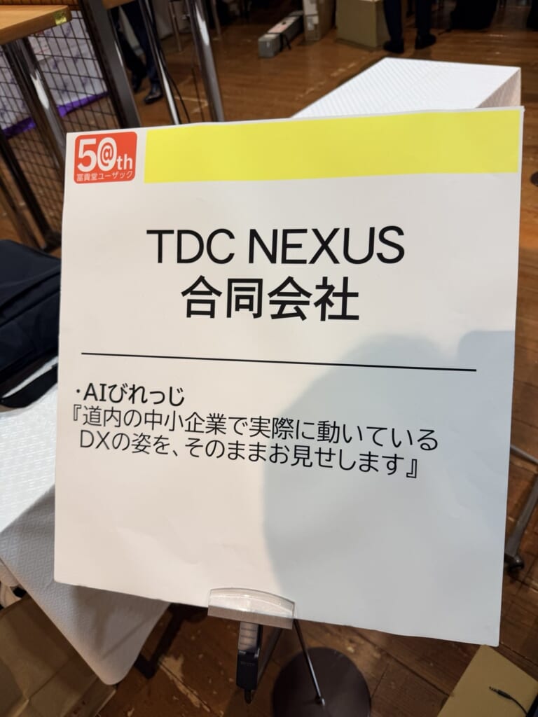 AIびれっじ TDC NEXUS合同会社のブース看板「道内の中小企業で実際に動いているDXの姿を、そのままお見せします」